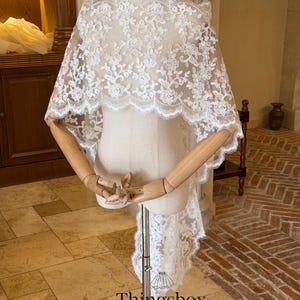 May include: A white lace bridal cape displayed on a mannequin. The cape features a floral pattern and scalloped edges. The text "Thingsbox Handmade Bridal Veils" is visible at the bottom of the image.