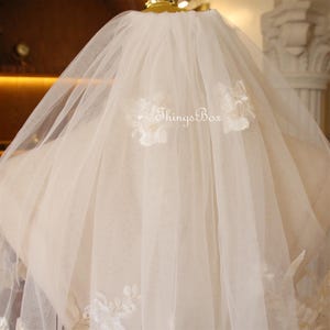 May include: A white bridal veil with delicate floral lace appliques. The veil is made of soft tulle and has a single layer.