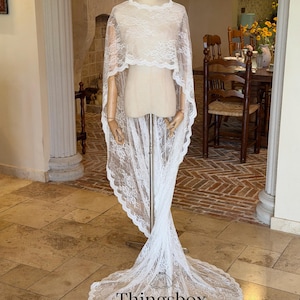 May include: A white lace bridal veil and cape set displayed on a mannequin. The set includes a short, scalloped-edge cape and a long veil with a matching lace trim. The text "Thingsbox Handmade Bridal Veils" is visible at the bottom.