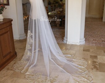 May include: A white bridal veil with a gold lace trim. The veil is long and flowing, and it is draped over a mannequin.