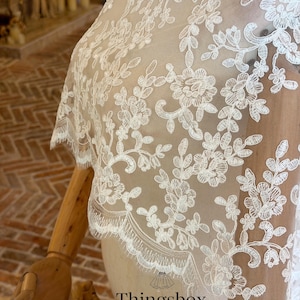 May include: Ivory lace bridal veil with floral and leaf patterns. The delicate lace features intricate embroidery and a scalloped edge. The veil is displayed on a mannequin, showcasing its design and texture. The text "Thingsbox Handmade Bridal Veils" is visible.