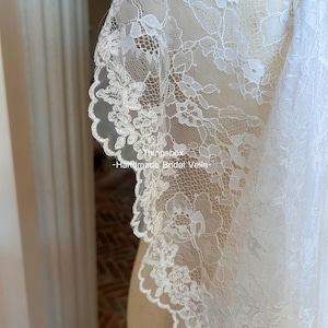 Może przedstawiać: Zbliżenie białego, koronkowego welonu ślubnego. Delikatna koronka ma kwiatowe wzory i falisty brzeg. Widoczny jest tekst "thingsbox - Handmade Bridal Veils".
