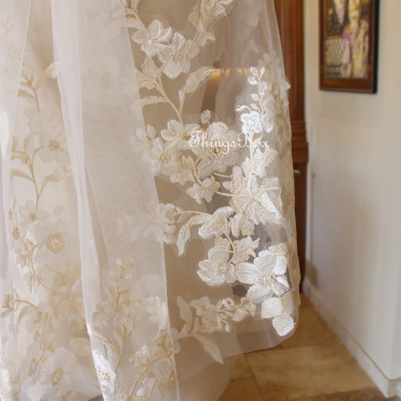 May include: Close-up of ivory tulle fabric with delicate floral embroidery. The embroidery is in a cream color and features a variety of flower shapes.