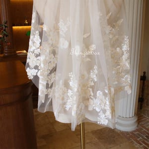 May include: A white bridal veil with delicate floral embroidery in a cream color. The veil is made of soft tulle and has a scalloped edge.