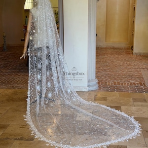 May include: A long, sheer white bridal veil featuring intricate silver embroidery of stars, moons, and celestial patterns. The veil has a scalloped edge with small star-shaped lace details and is displayed on a mannequin. Text reads Thingsbox.