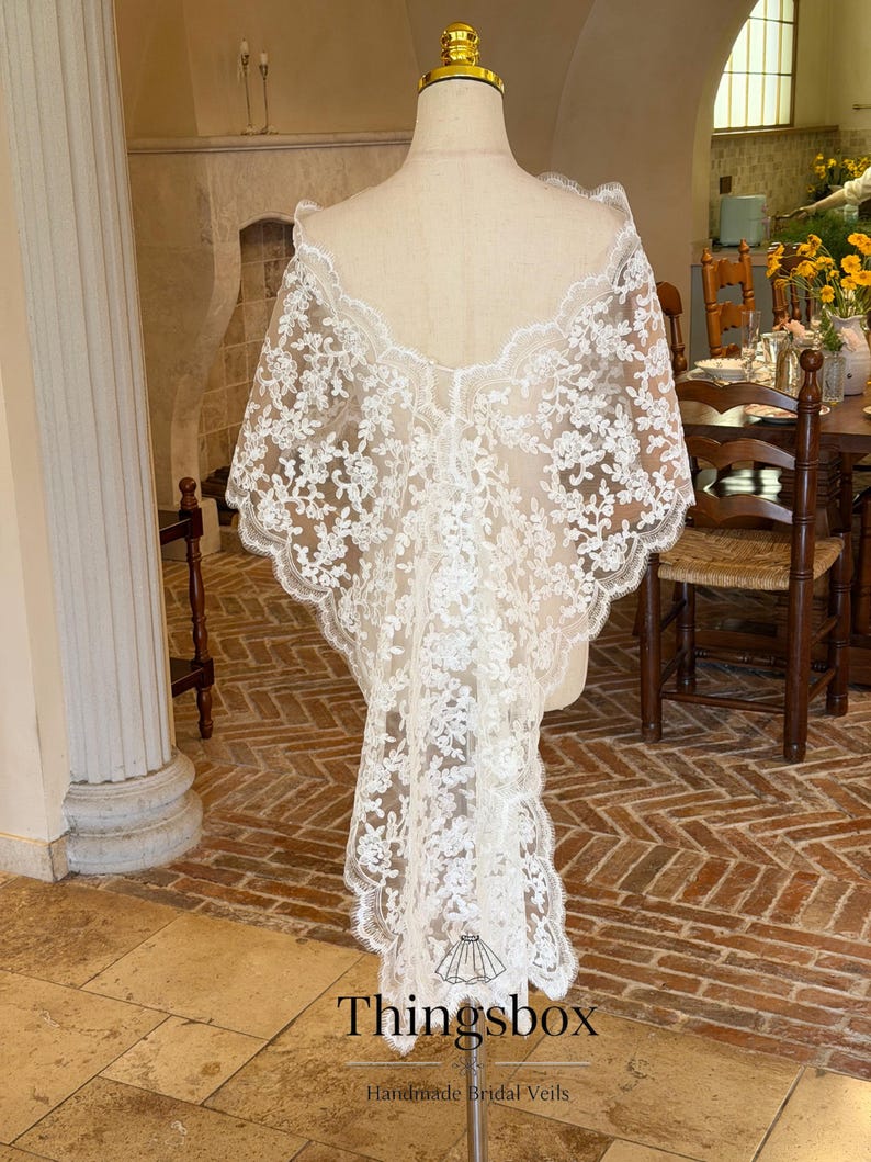 May include: A white lace bridal veil with floral patterns is draped over a mannequin. The veil has a scalloped edge and a flowing design. The text "Thingsbox" and "Handmade Bridal Veils" are visible at the bottom.