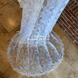 Może przedstawiać: Biały koronkowy welon ślubny z falistym brzegiem. Welon jest udrapowany na kafelkowanej powierzchni. Tekst "Thingsbox Handmade Bridal Veils" jest widoczny na zdjęciu.