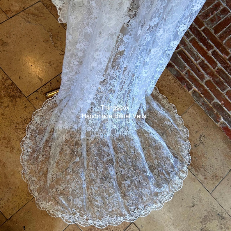 Może przedstawiać: Biały koronkowy welon ślubny z falistym brzegiem. Welon jest udrapowany na kafelkowanej powierzchni. Tekst "Thingsbox Handmade Bridal Veils" jest widoczny na zdjęciu.