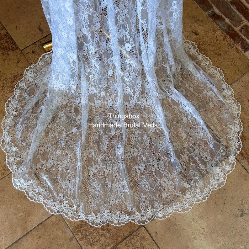 Może przedstawiać: Biały welon ślubny z koronki z falistym brzegiem. Welon wykonany jest z delikatnej koronki z kwiatowym wzorem. Widoczny jest tekst "Thingsbox Handmade Bridal Veils".