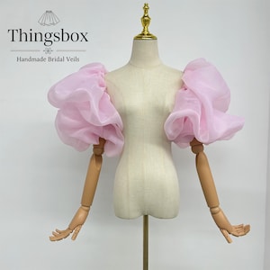 May include: A pair of pink tulle puff sleeves. The sleeves are attached to wooden arms, which are attached to a white mannequin.