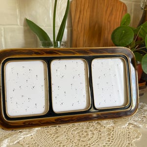 May include: A rectangular triple photo frame with a tortoiseshell pattern. The frame has three openings with white backgrounds and black borders, and a gold trim. The frame is sitting on a white surface.