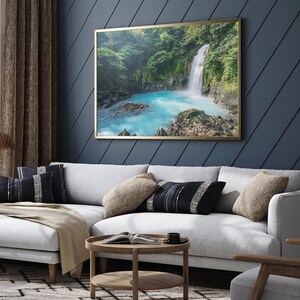 a large framed picture of a waterfall hanging on a blue wall in a living room.