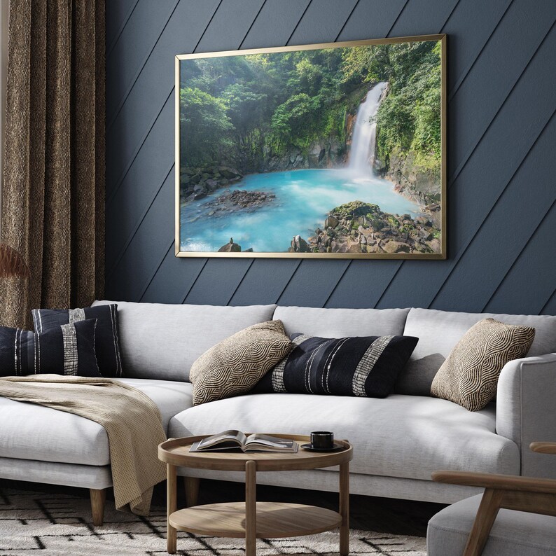 a large framed picture of a waterfall hanging on a blue wall in a living room.