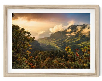 Puede incluir: Una fotografía de paisaje enmarcada que muestra un valle montañoso verde al atardecer. La escena incluye picos escarpados parcialmente ocultos por nubes, con luz dorada iluminando las crestas y el follaje en tonos verdes y rojos.