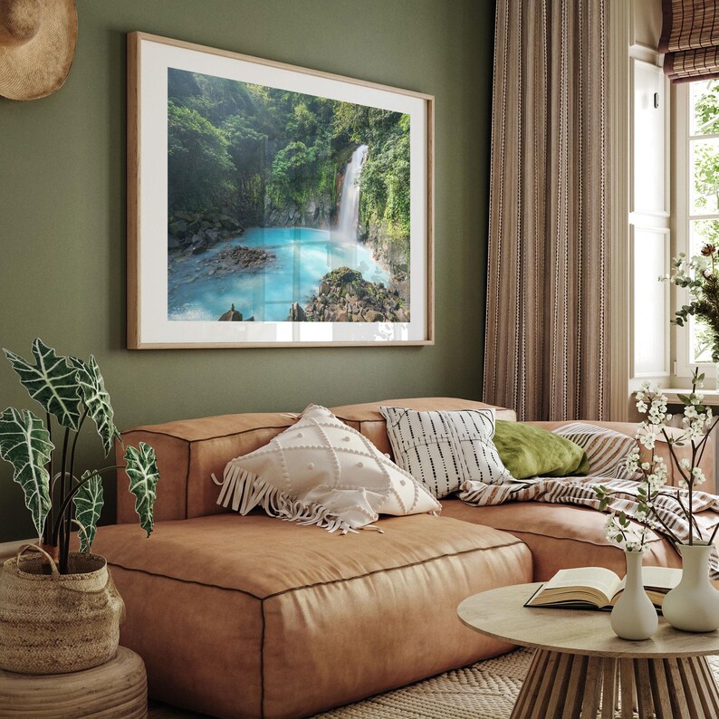 a large framed picture of a waterfall hanging on a green wall in a living room.