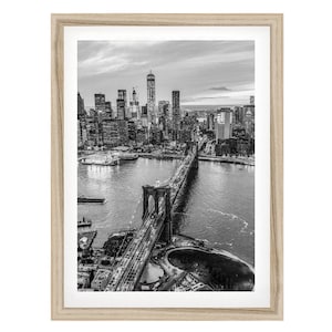 A black and white aerial view of the Brooklyn Bridge and the New York City skyline, with the bridge spanning the East River.