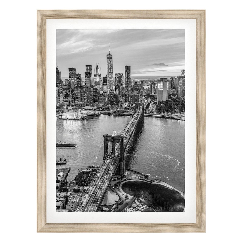 A black and white aerial view of the Brooklyn Bridge and the New York City skyline, with the bridge spanning the East River.
