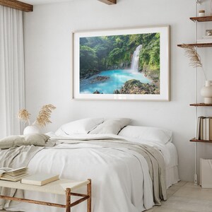 a serene bedroom scene with a large framed picture of a waterfall hanging on the wall above a bed with white linens and pillows.