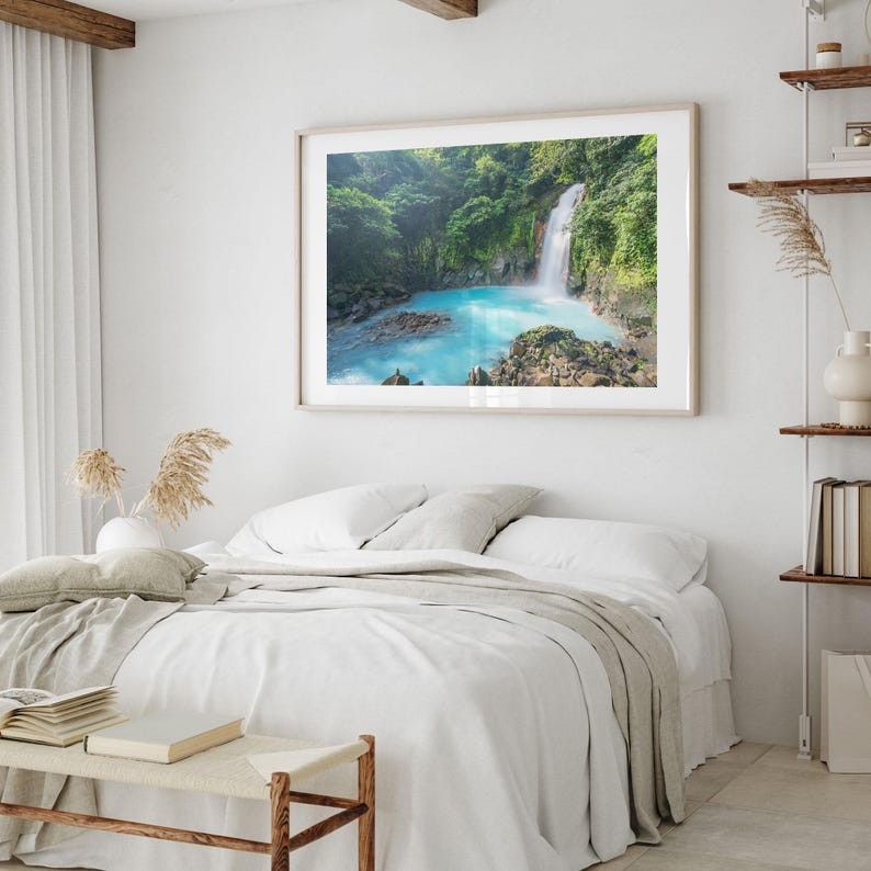 a serene bedroom scene with a large framed picture of a waterfall hanging on the wall above a bed with white linens and pillows.
