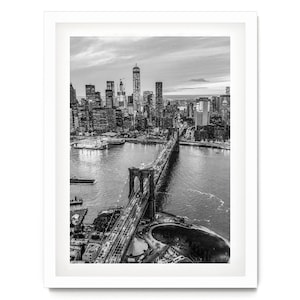 A black and white aerial view of the Brooklyn Bridge and the surrounding cityscape of New York City.