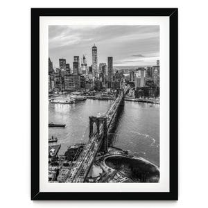 A black and white aerial view of the Brooklyn Bridge and the surrounding cityscape of New York City.