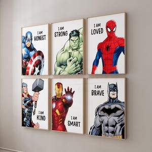 May include: Six framed superhero art prints. Each print features a different superhero with a motivational phrase: "I AM HONEST", "I AM STRONG", "I AM LOVED", "I AM KIND", "I AM SMART", and "I AM BRAVE". The prints are in a light-coloured wooden frame.