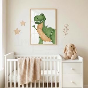 May include: A framed print featuring a friendly green Tyrannosaurus Rex illustration with a tan belly. The artwork is in a light wood frame, hanging above a white crib with a beige blanket. A stuffed bunny sits on a white dresser.