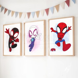 May include: Three framed cartoon prints featuring Spider-Man characters. The prints showcase Spider-Man, Spider-Gwen, and Miles Morales in action poses, with a colorful banner above. The artwork is set against a white wall.