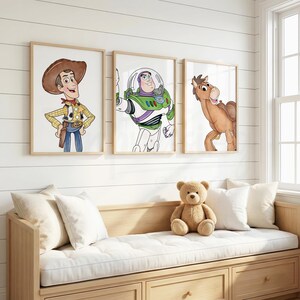 May include: Three framed watercolor prints featuring characters from the Toy Story movie. Woody, Buzz Lightyear, and Bullseye are depicted in a child's bedroom setting. A wooden bench with a white cushion and pillows is below the prints.