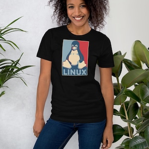 May include: Black t-shirt featuring a penguin graphic in a red, blue, and beige color scheme. The word "LINUX" is printed below the penguin. The shirt is made of a soft material.