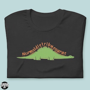 Pode incluir: Camiseta preta com uma ilustração de dinossauro verde e o texto "Normaldistribusaurus" em laranja. O dinossauro é uma representação estilizada de um Brontosaurus. A camiseta tem gola redonda e mangas curtas.