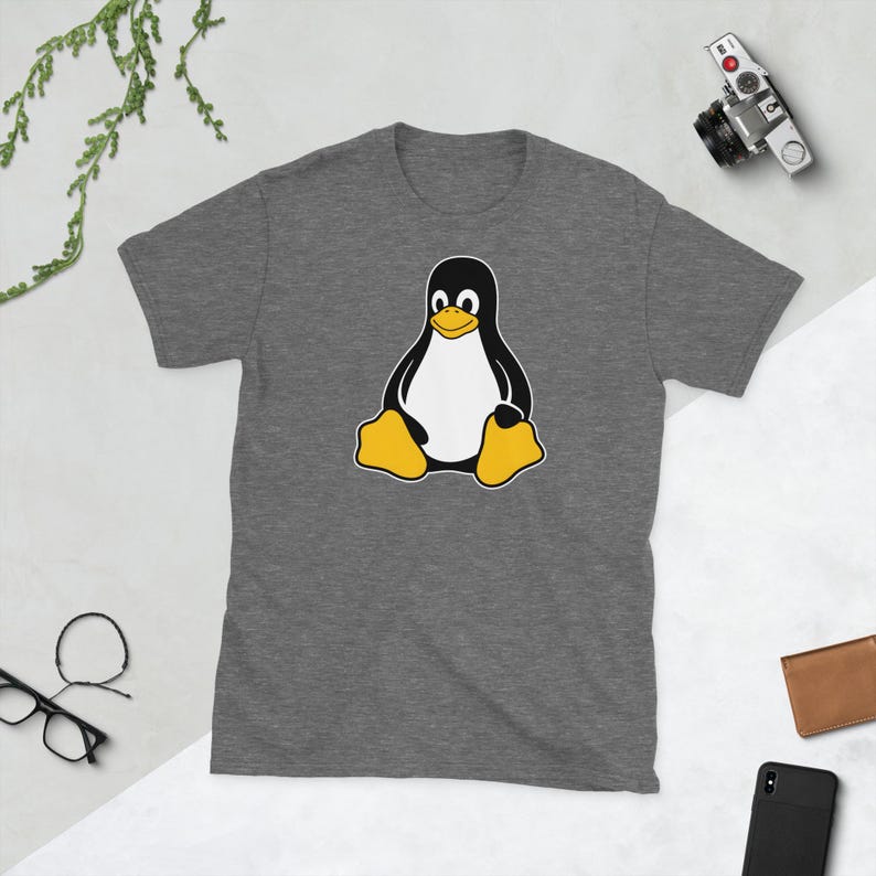 Puede incluir: Camiseta gris jaspeado con un dise&ntilde;o de ping&uuml;ino de dibujos animados. El ping&uuml;ino tiene un cuerpo negro, vientre blanco, pies amarillos y pico amarillo. El ping&uuml;ino est&aacute; sentado. La camiseta es de material suave.