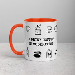Op de afbeelding: Witte keramische koffiemok met een oranje binnenkant en oor. De mok is versierd met zwarte lijntekeningen van koffie-items en de tekst "I DRINK COFFEE IN MODERATION."