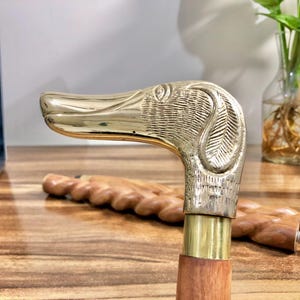 May include: A brass walking stick with a dog head handle. The handle is detailed with a textured finish and the stick is made of wood.