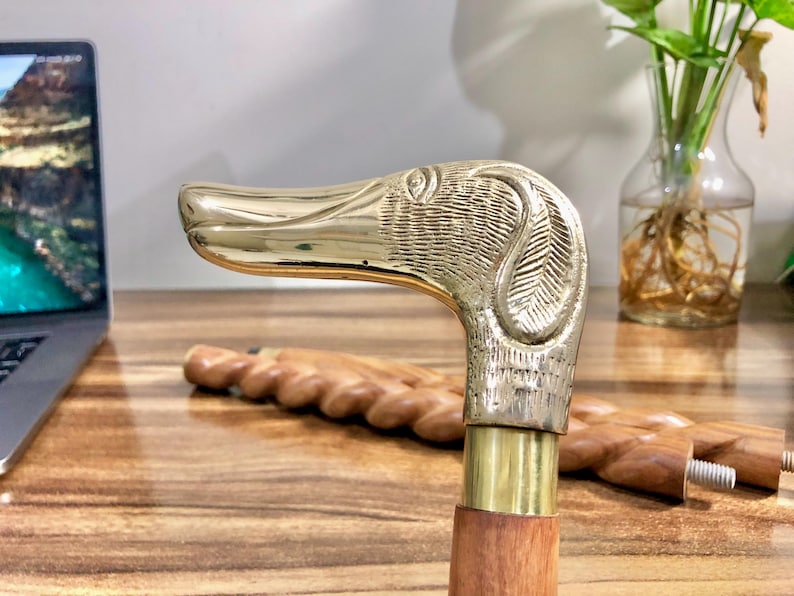 May include: A brass walking stick with a dog head handle. The handle is detailed with a textured finish and the stick is made of wood.