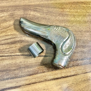 May include: Silver-toned metal walking stick handle with a detailed dog head design. The handle is curved and has a ring on the side.