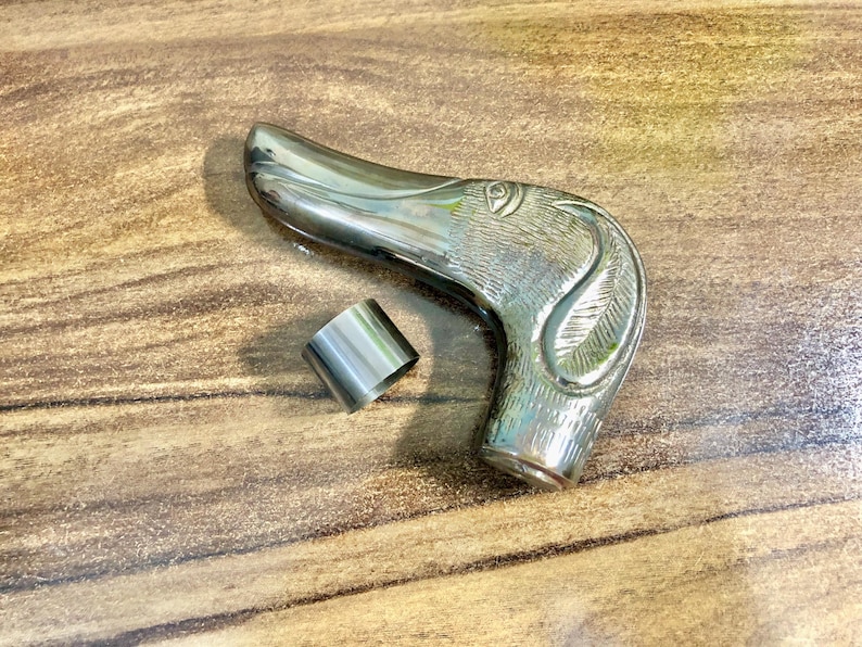 May include: Silver-toned metal walking stick handle with a detailed dog head design. The handle is curved and has a ring on the side.