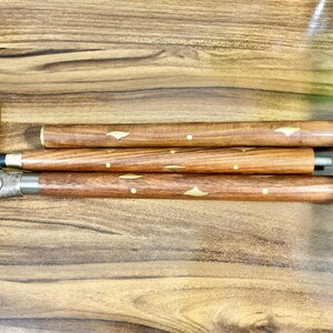 May include: A wooden walking stick with a decorative metal handle. The stick is made of three sections that can be unscrewed and assembled. The sections are decorated with brass inlays.