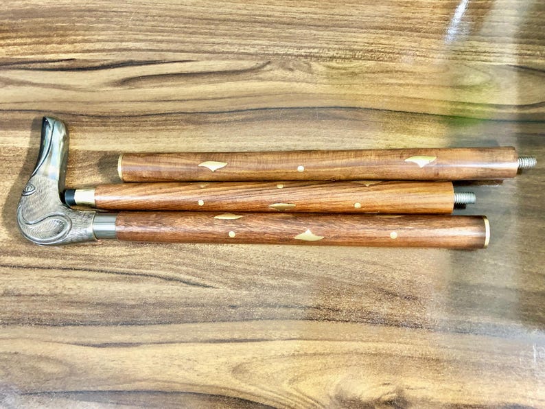 May include: A wooden walking stick with a decorative metal handle. The stick is made of three sections that can be unscrewed and assembled. The sections are decorated with brass inlays.