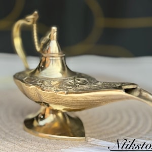 K&ouml;nnte beinhalten: Eine goldfarbene Dschinnenlampe mit filigranen Details und einem gebogenen Ausguss. Die Lampe ist aus Metall und hat ein traditionelles Design.