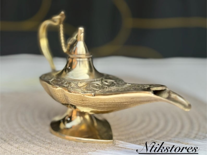 K&ouml;nnte beinhalten: Eine goldfarbene Dschinnenlampe mit filigranen Details und einem gebogenen Ausguss. Die Lampe ist aus Metall und hat ein traditionelles Design.