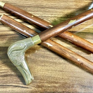 May include: A wooden walking stick with a brass handle shaped like a bird's head. The stick has gold accents and a brown finish.