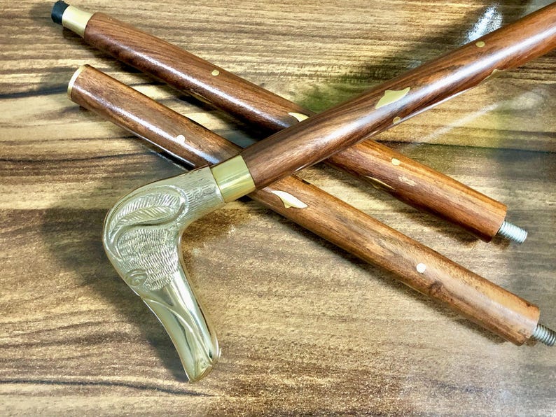 May include: A wooden walking stick with a brass handle shaped like a bird's head. The stick has gold accents and a brown finish.