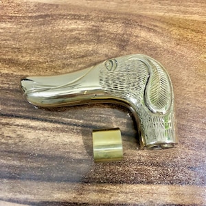 May include: A gold-colored metal walking stick handle with a detailed dog head design. The handle is smooth and polished.