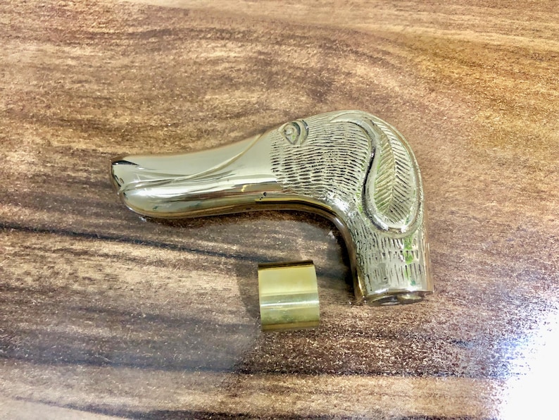 May include: A gold-colored metal walking stick handle with a detailed dog head design. The handle is smooth and polished.