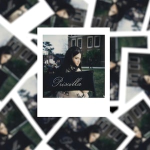 May include: A black and white photo of a woman sitting on a director's chair with the name "Priscilla" written on it. The woman is wearing a white coat and has dark hair. The photo is in a white frame.