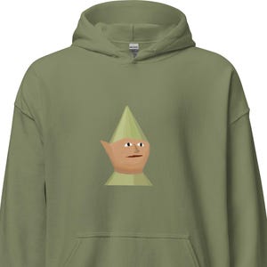 Pode incluir: Moletom com capuz verde-oliva com um rosto de gnomo de desenho animado. O gnomo tem um chapéu verde, um rosto castanho e uma gola verde. O moletom tem um bolso canguru e um capuz com cordão.