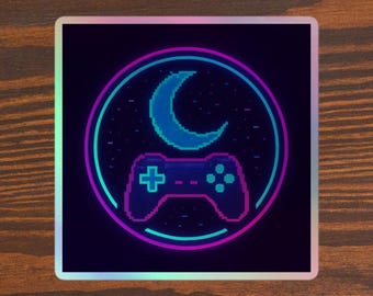 May include: Square sticker with a neon design featuring a crescent moon, stars, and a video game controller. The design is in shades of blue, purple, and pink, with a black background. The sticker is on a wooden surface.