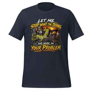 May include: A navy blue t-shirt featuring a graphic of a skeleton in a high-visibility jacket and cap, relaxing in a chair while holding a drink. The text reads: LET ME STOP WHAT I'M DOING AND WORK ON YOUR PROBLEM, with NOT MY CIRCUS NOT MY MONKEYS.