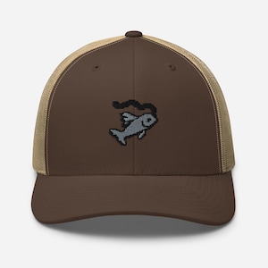 May include: A brown baseball cap with a tan mesh back and an adjustable snapback closure. The front panel features an embroidered pixel art design of a grey fish with a black line trailing above it, centered on the solid brown fabric surface.